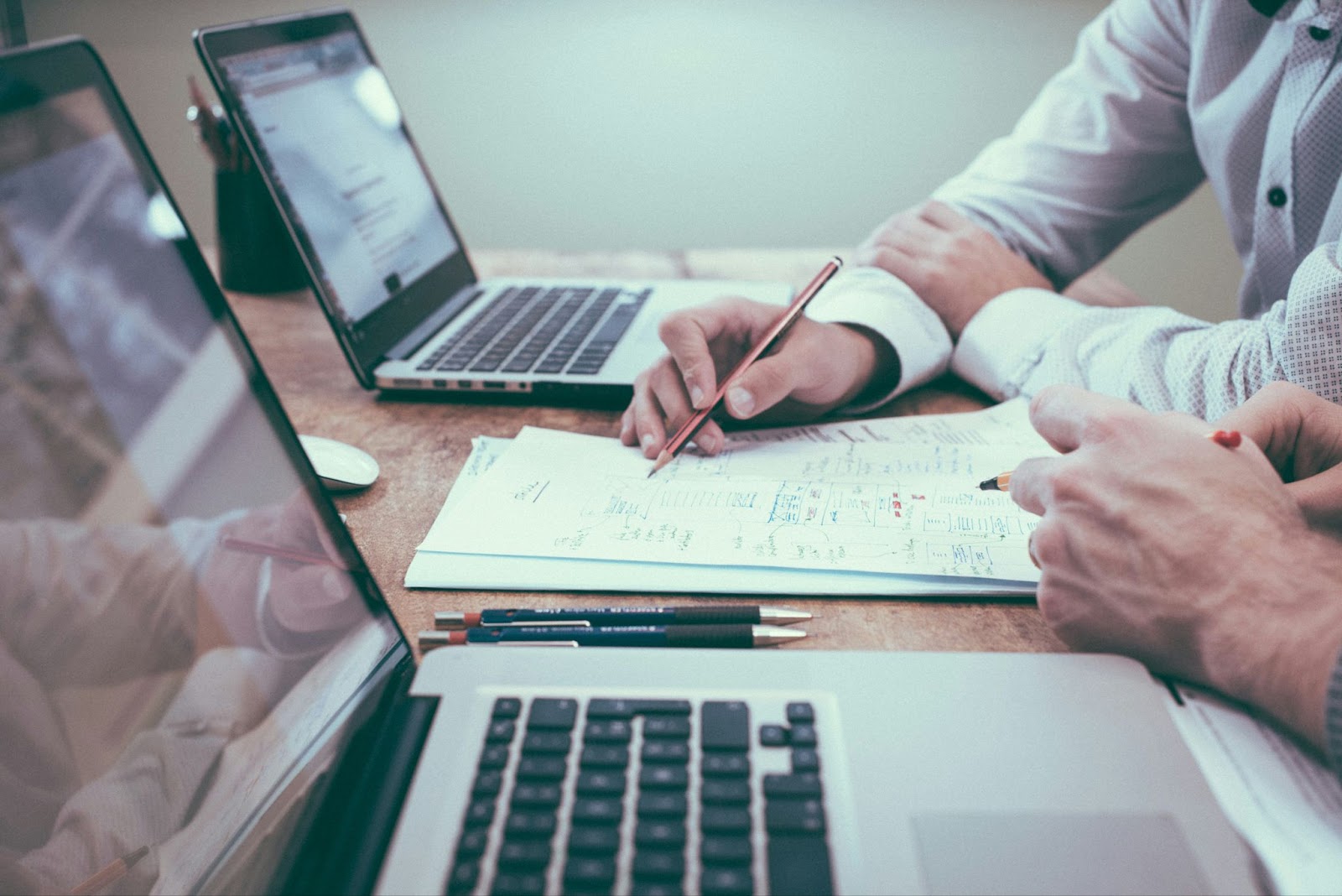 Personas trabajando en equipo con computadoras portátiles y revisando documentos sobre una mesa