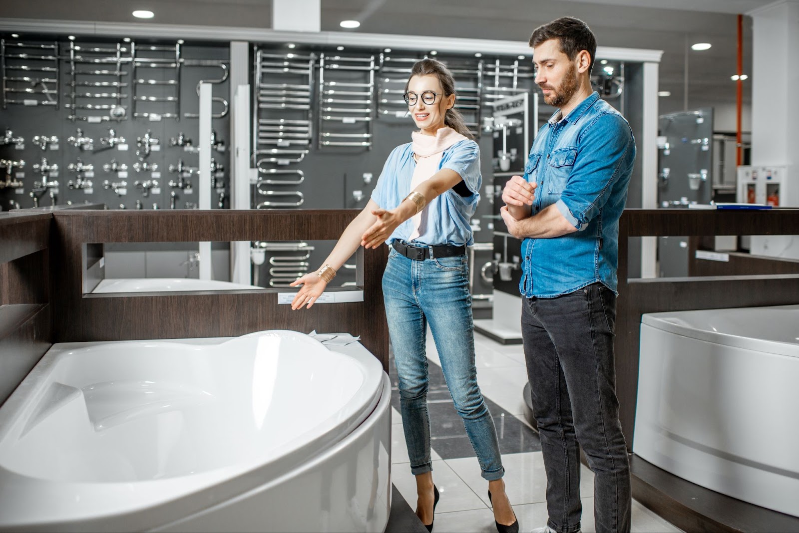 A couple selecting a new bathtub in a store, with the wife measuring the tub's size with her hands.