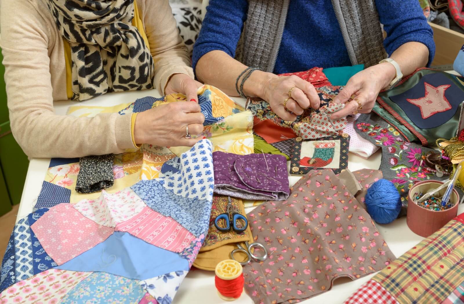 Two seniors at a table covered in different fabrics, threads, and scissors as they begin a quilting project