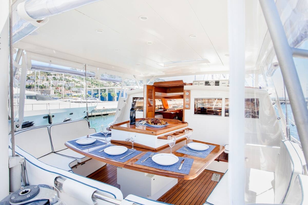 white cushions surrounding a brown table with plans and silver wear set up op on the deck of a boat 