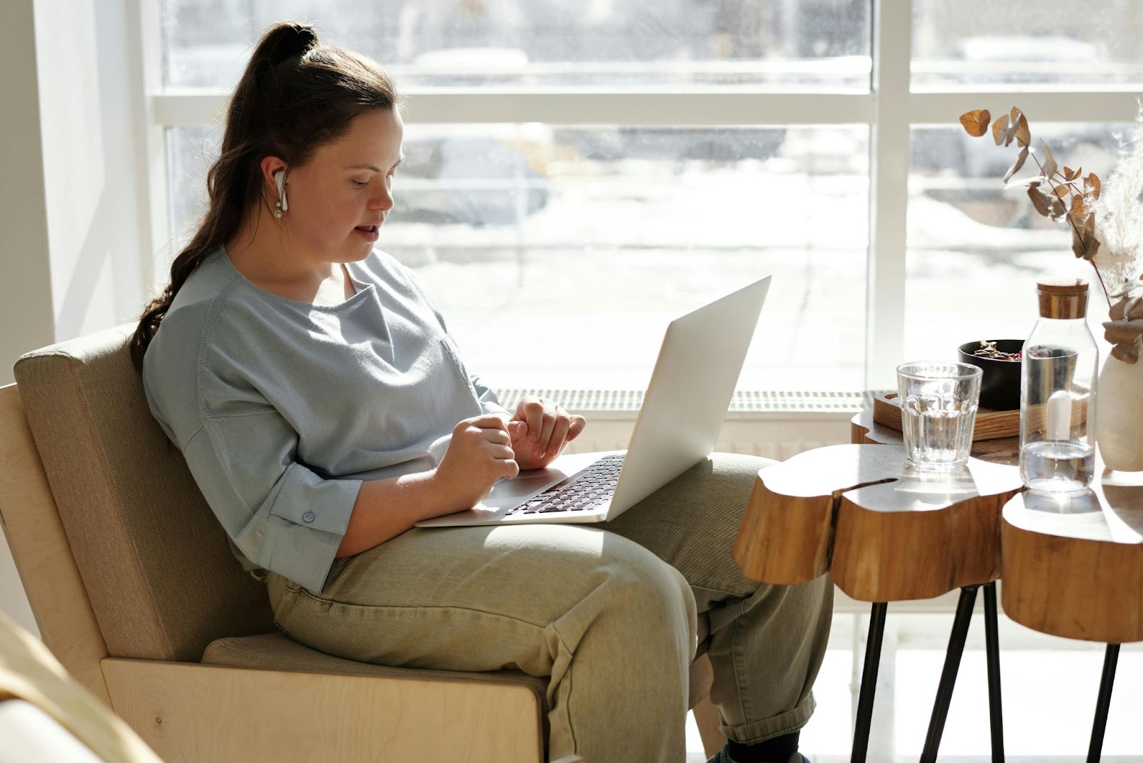 A woman sitting in a chair near a window working on her laptop