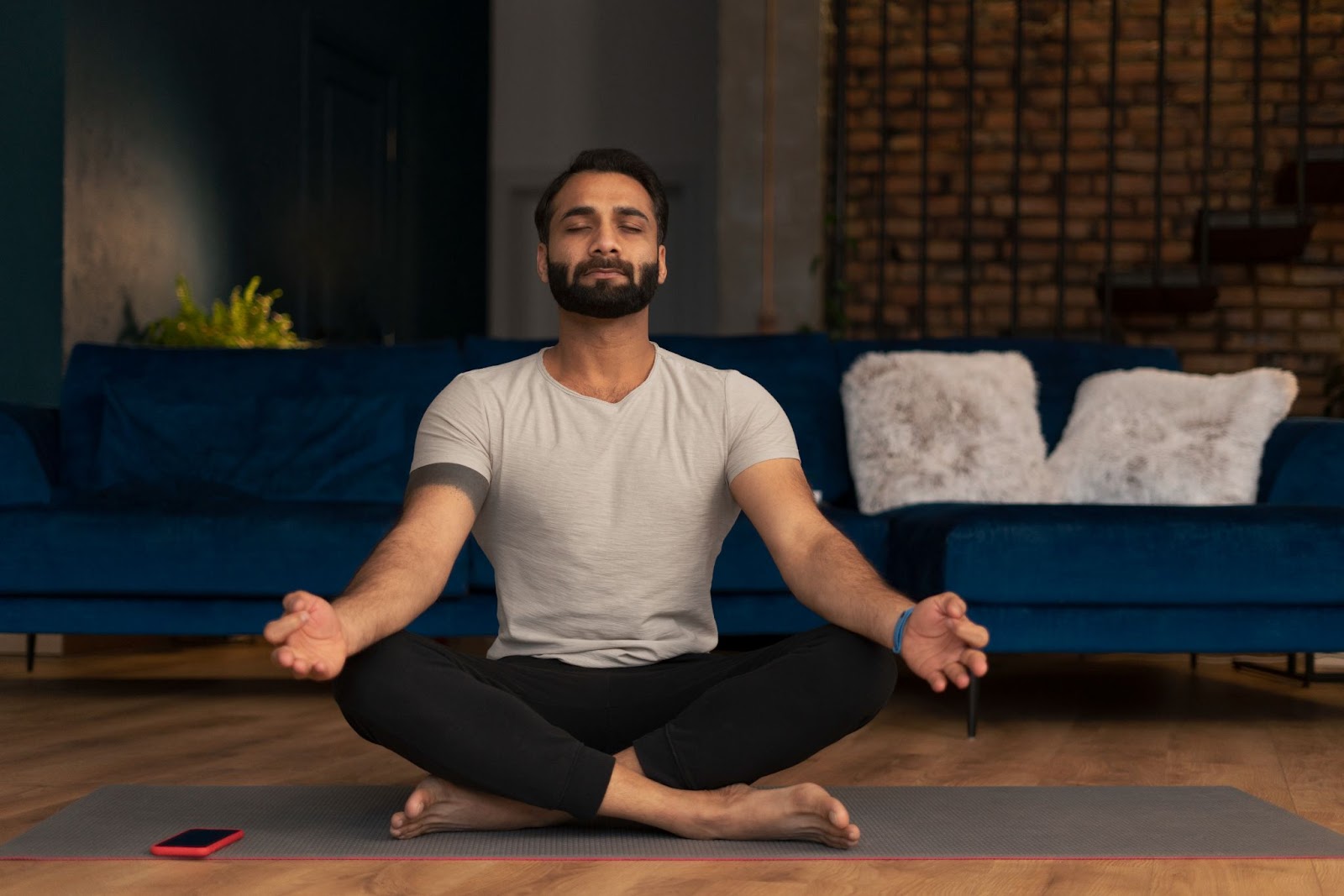 A man meditates on a yoga mat in his living room.