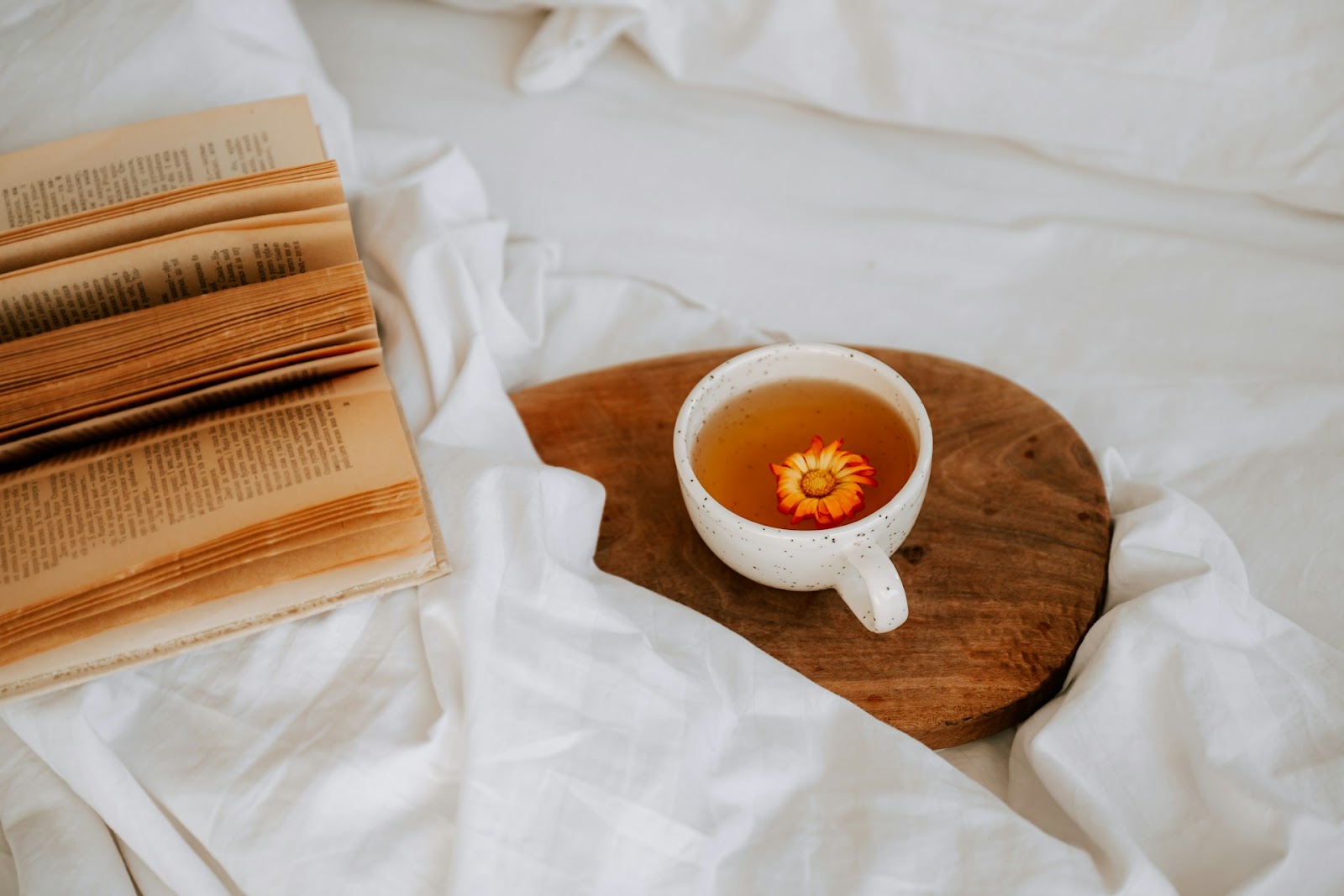 A sleep tea in a bed next to a book, a flower floating on the water