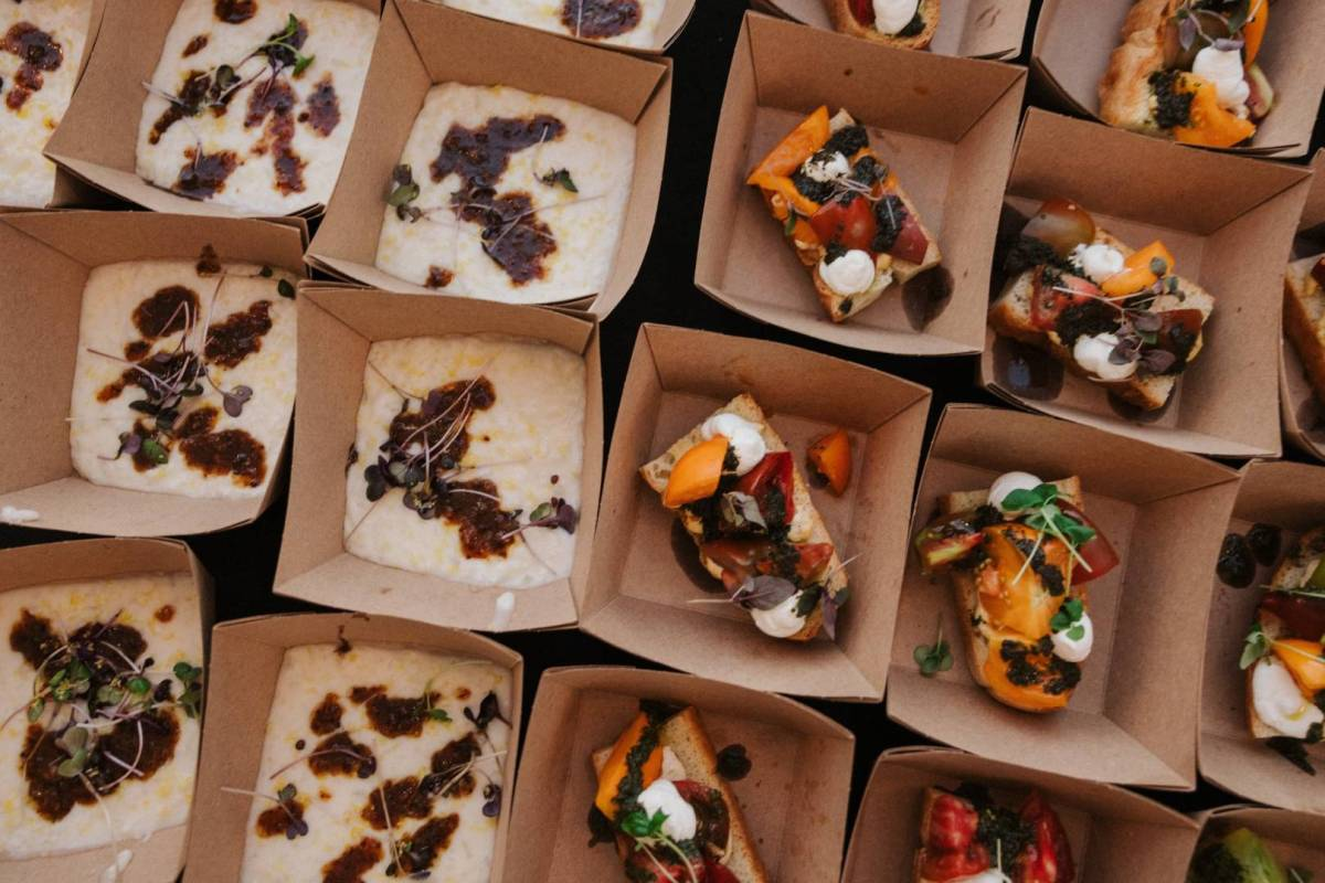 An overhead shot of a dozen dishes in paper take-out containers