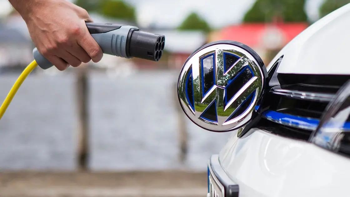 En hand, hållandes en AC-laddkontakt framför en Volkswagen