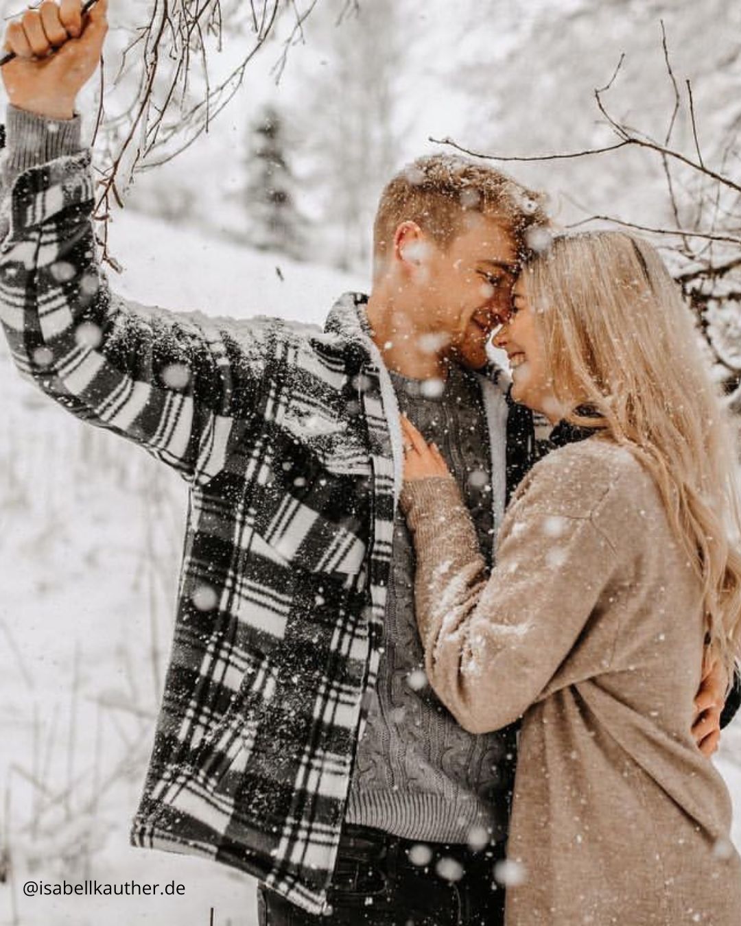 winter engagement photos a couple hugs under a snow covered tree