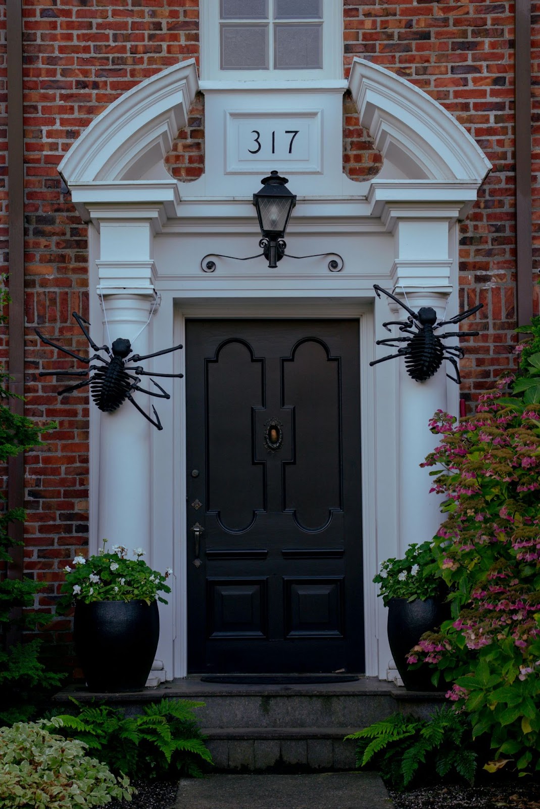 The front door of a brick house with two giant black plastic spider decorations on either side