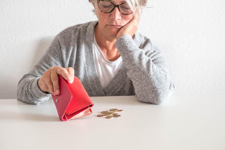 An aged lady with a purse staring at coins on the table