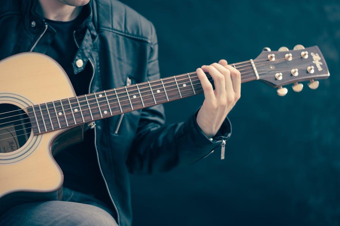 Free Close-up of a musician playing an acoustic guitar, wearing a leather jacket. Stock Photo