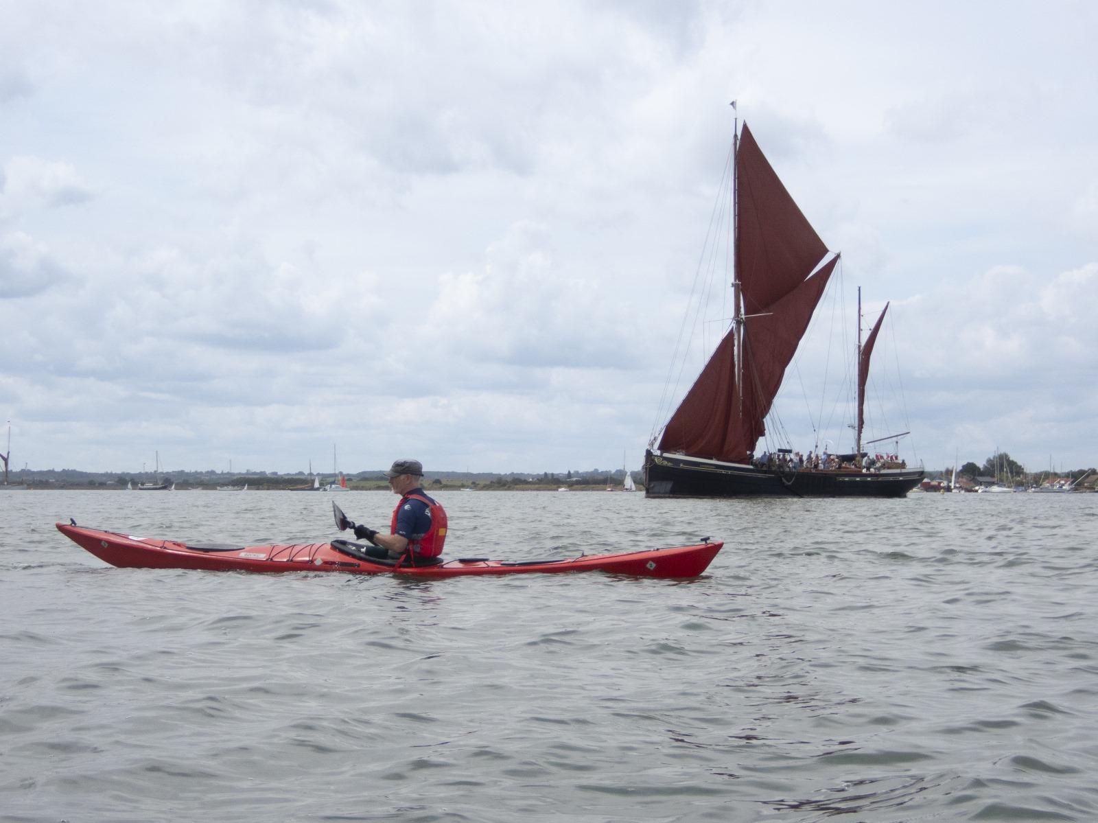 A person in a kayak and a sailboat

Description automatically generated