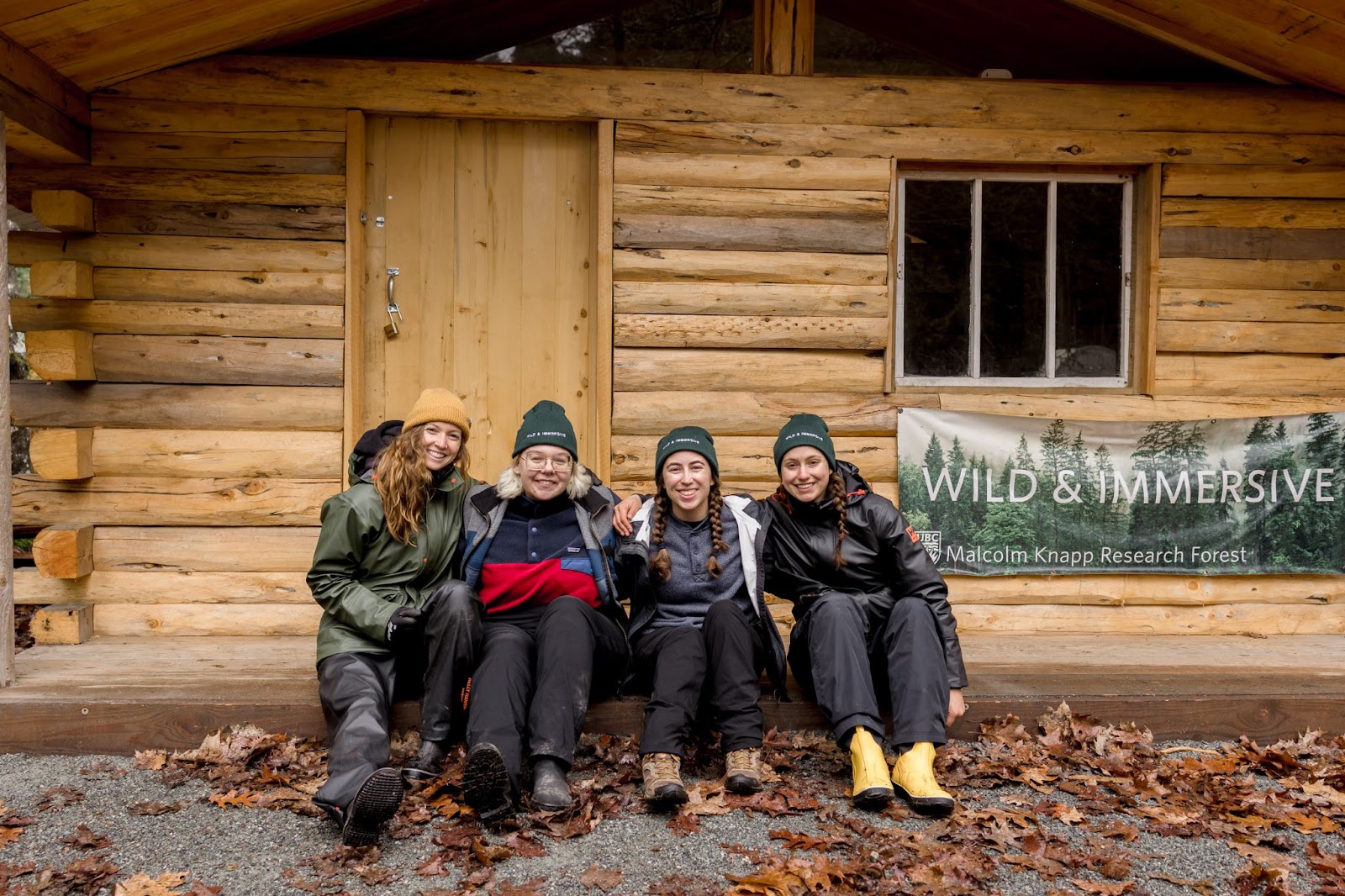 Four team members of Wild & Immersive sitting on the front porch of a wooden cabin with a sign in the background. 