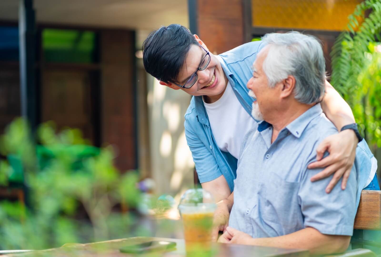 An adult son & his senior father enjoying a smoothie together at a senior living community.