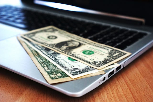 Three US dollar bills sitting on an open laptop 