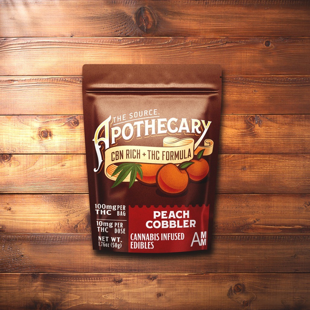 The Source Apothecary Cannabinoid Rich formula Peach Cobbler cannabis edibles are enriched with the alternative cannabinoid CBN plus THC. The brown and orange kraft paper packaging is shown from above and the background is multicolored wood.