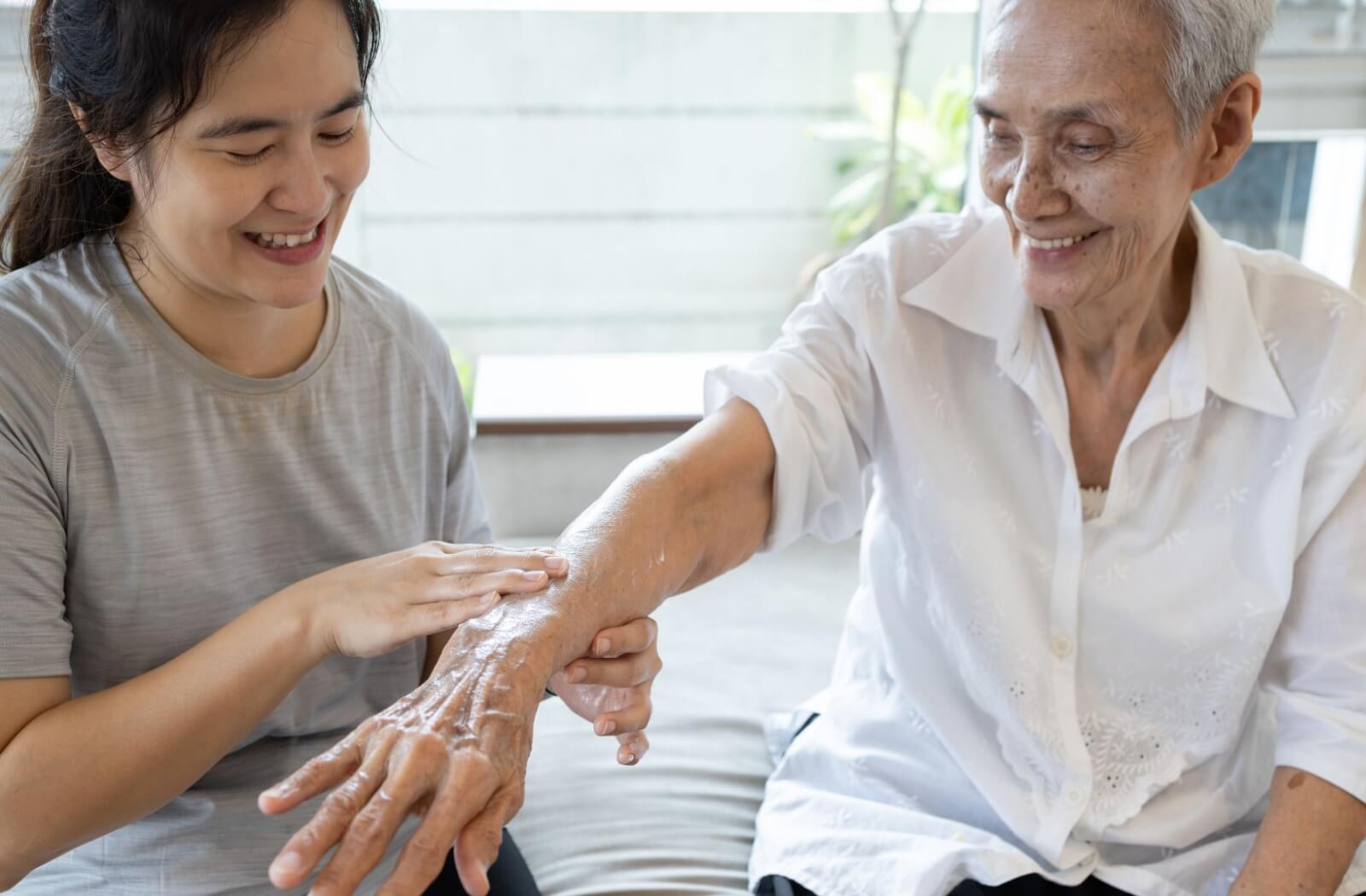  A smiling senior with dementia receives a hand massage from a caregiver as a stimulating activity