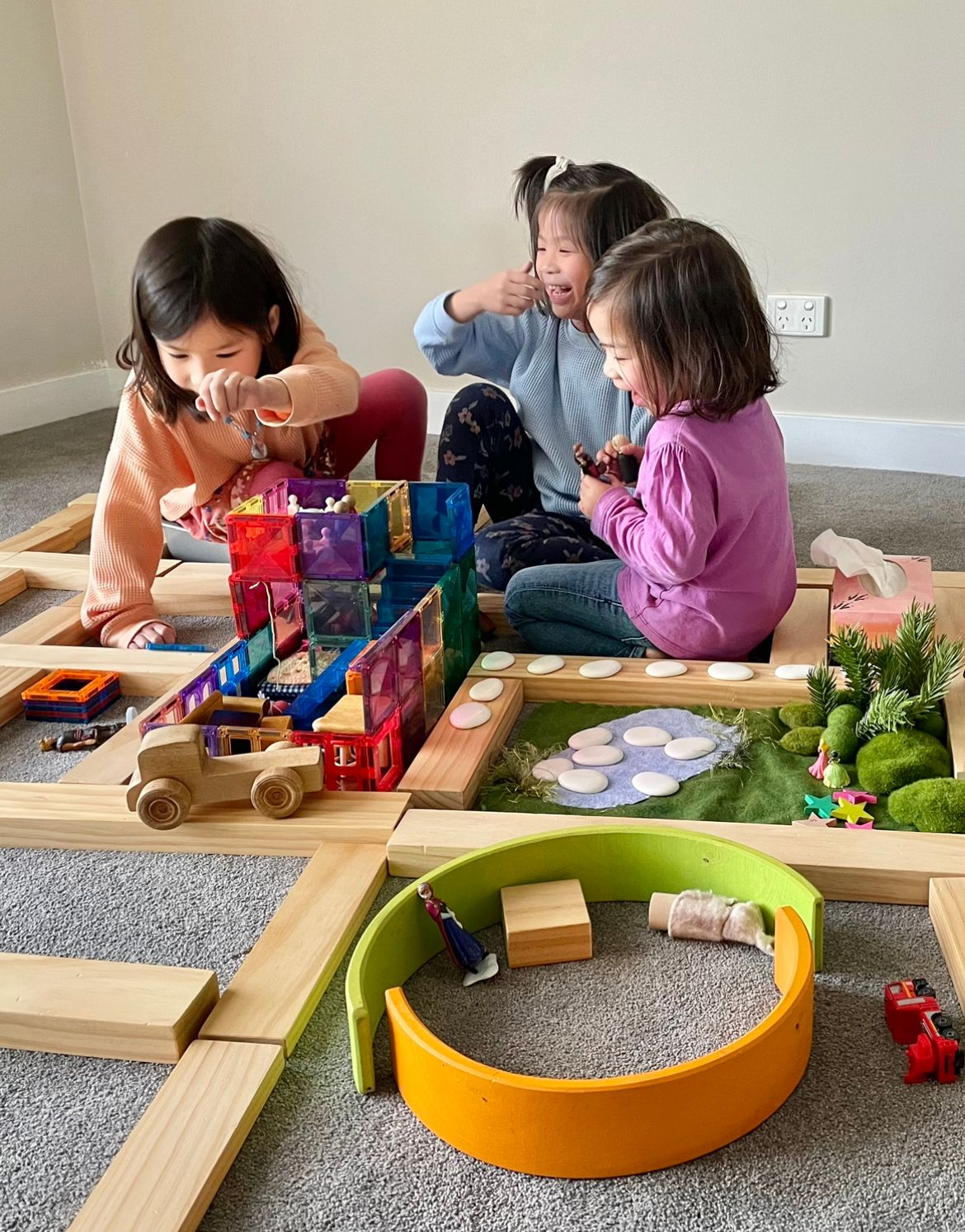 Siblings are happily playing together, sharing ideas as they create a story scene with colorful magnetic tiles. They engage in imaginative play, collaborating and communicating as they build structures and characters, fostering creativity and connection through their shared narrative.
