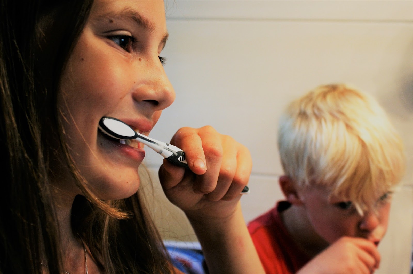 Two kids happily brush their teeth together in front of a mirror, promoting good oral hygiene habits.