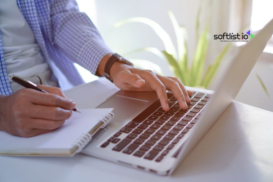 Person taking notes while using a laptop.