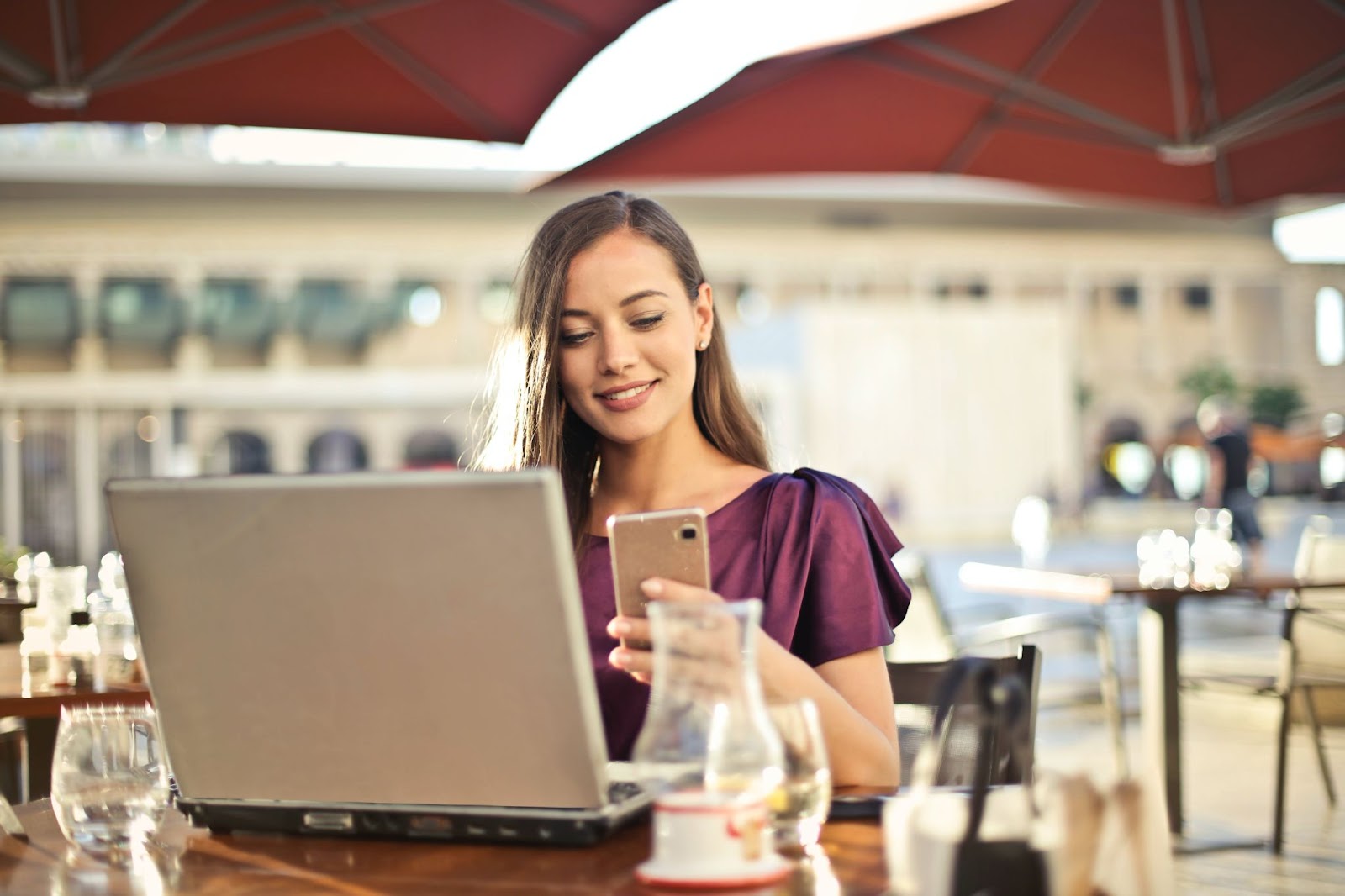 woman at a cafe holding her phone with laptop