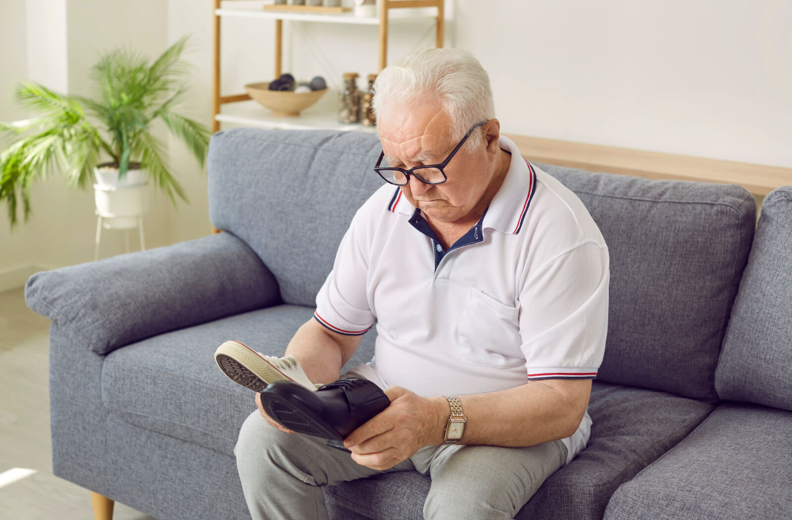 An older adult sitting on the couch comparing 2 pairs of new shoes.