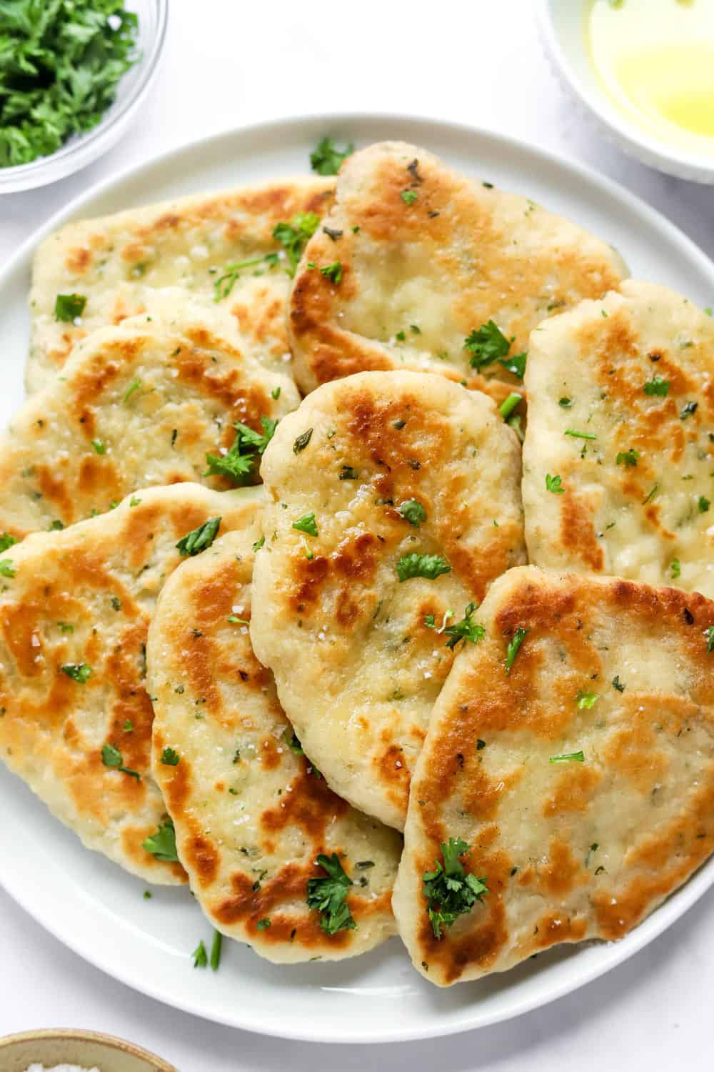 Pile of gluten free naan bread on a white plate topped with some oil and chopped parsley.