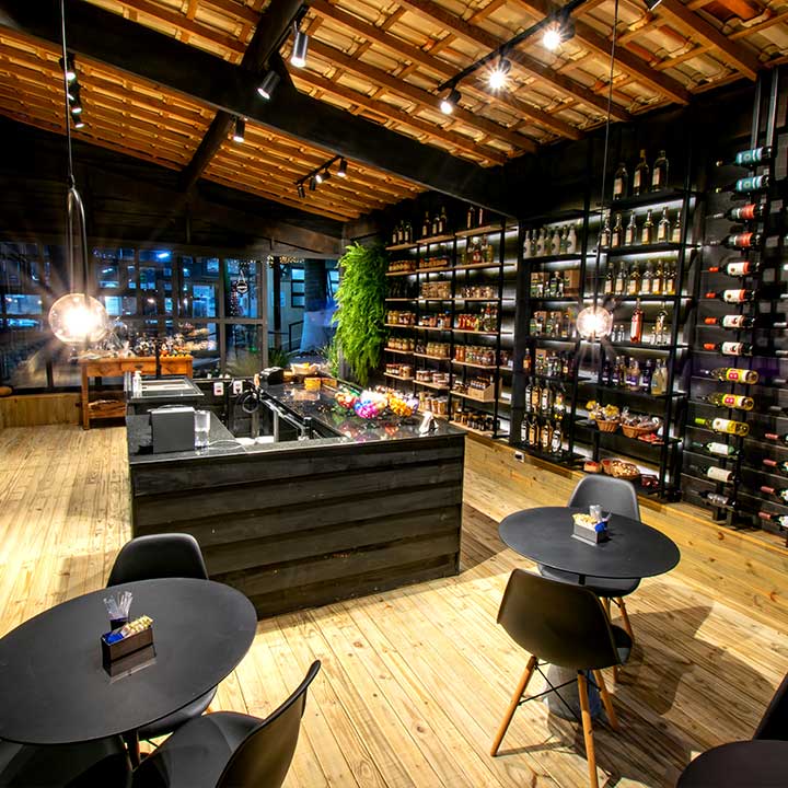 Detalhes de uma adega moderna com prateleiras de vinhos, mesa de bar, cadeiras pretas e iluminação aconchegante, ideal para apreciar vinhos em um ambiente sofisticado.