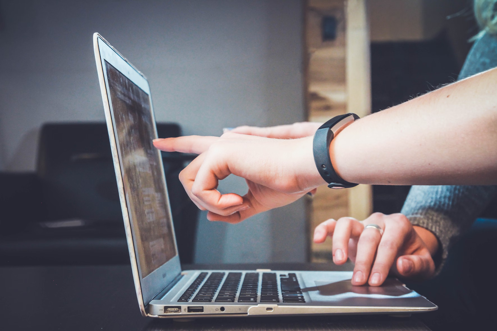 A laptop on a desk with someone pointing at the screen.