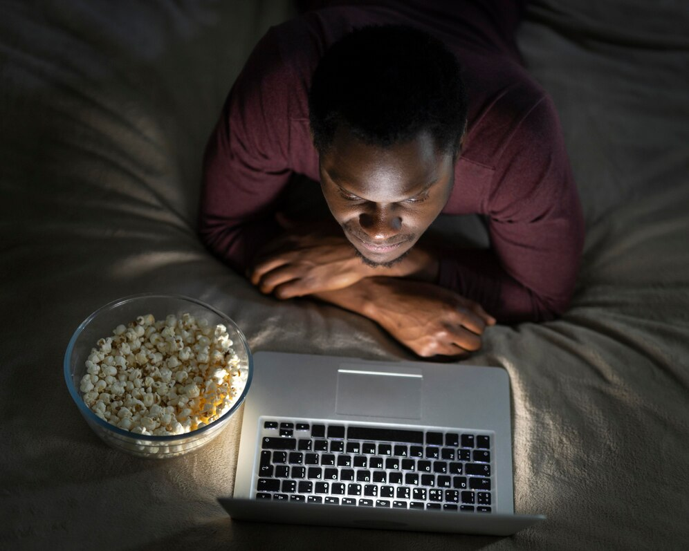 A man focused on his screen, watching a movie with popcorn due to YouTube addiction.