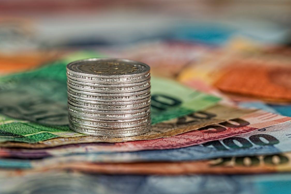 Free A stack of coins on top of various colored banknotes, symbolizing finance and currency. Stock Photo