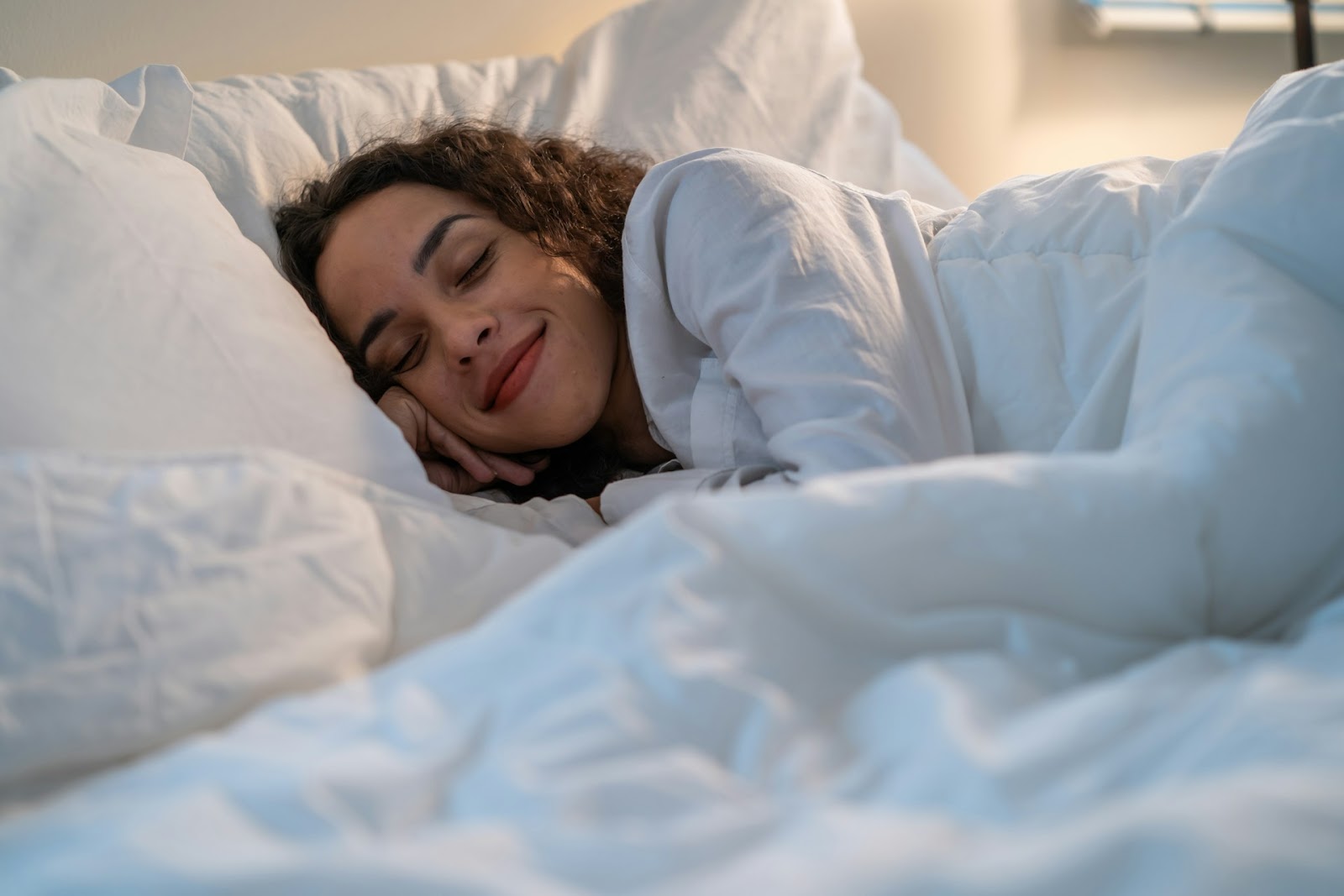 A woman wrapped up in duvets, ready to sleep, with a big smile on her face