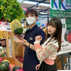 This contain Giselle  and Jihoon  wearing masks standing in front of produce at a grocery store with vegetables on display