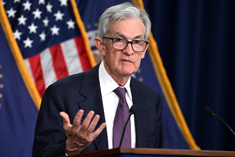 The chair of the Federal Reserve gestures at a podium, while standing in front of an American flag.