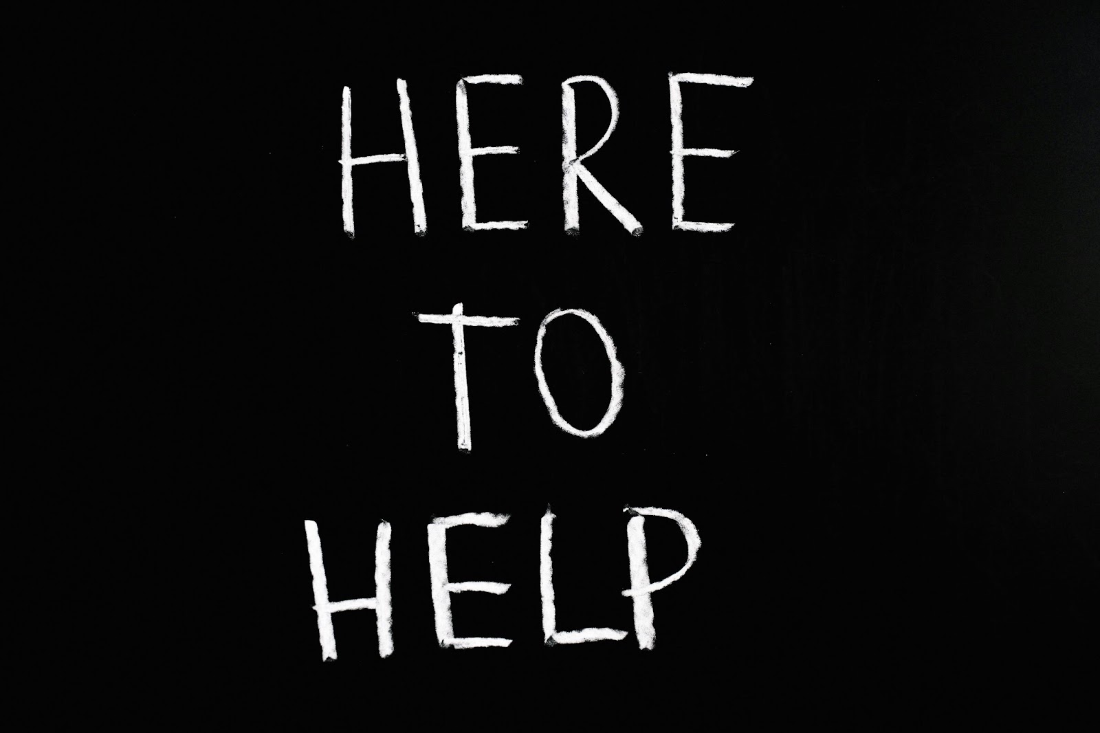 The phrase 'Here to Help' written in bold white chalk like letters on a black background