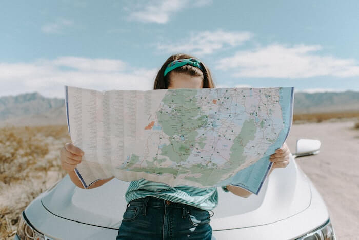 Woman looking at map, sitting on the hood of a white car