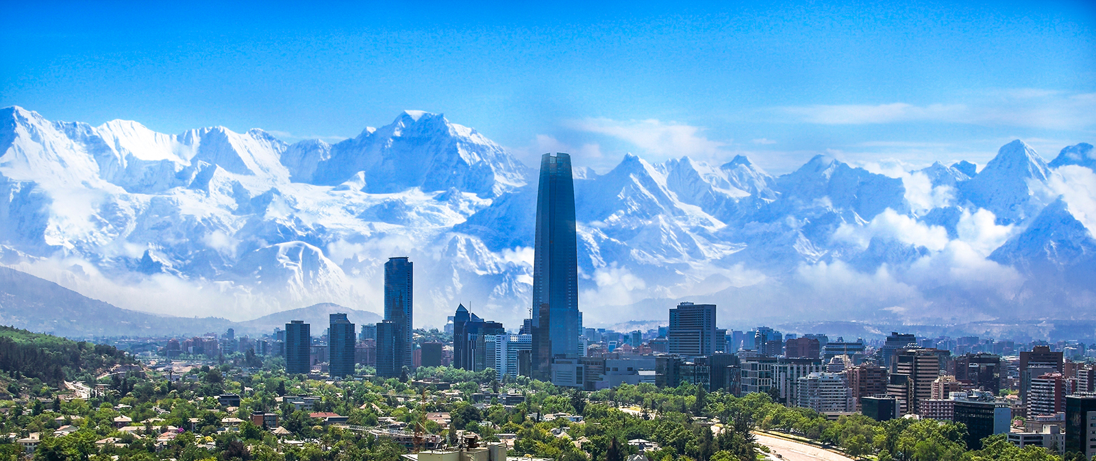 Skyline of tall buildings with snowy mountains in the background.