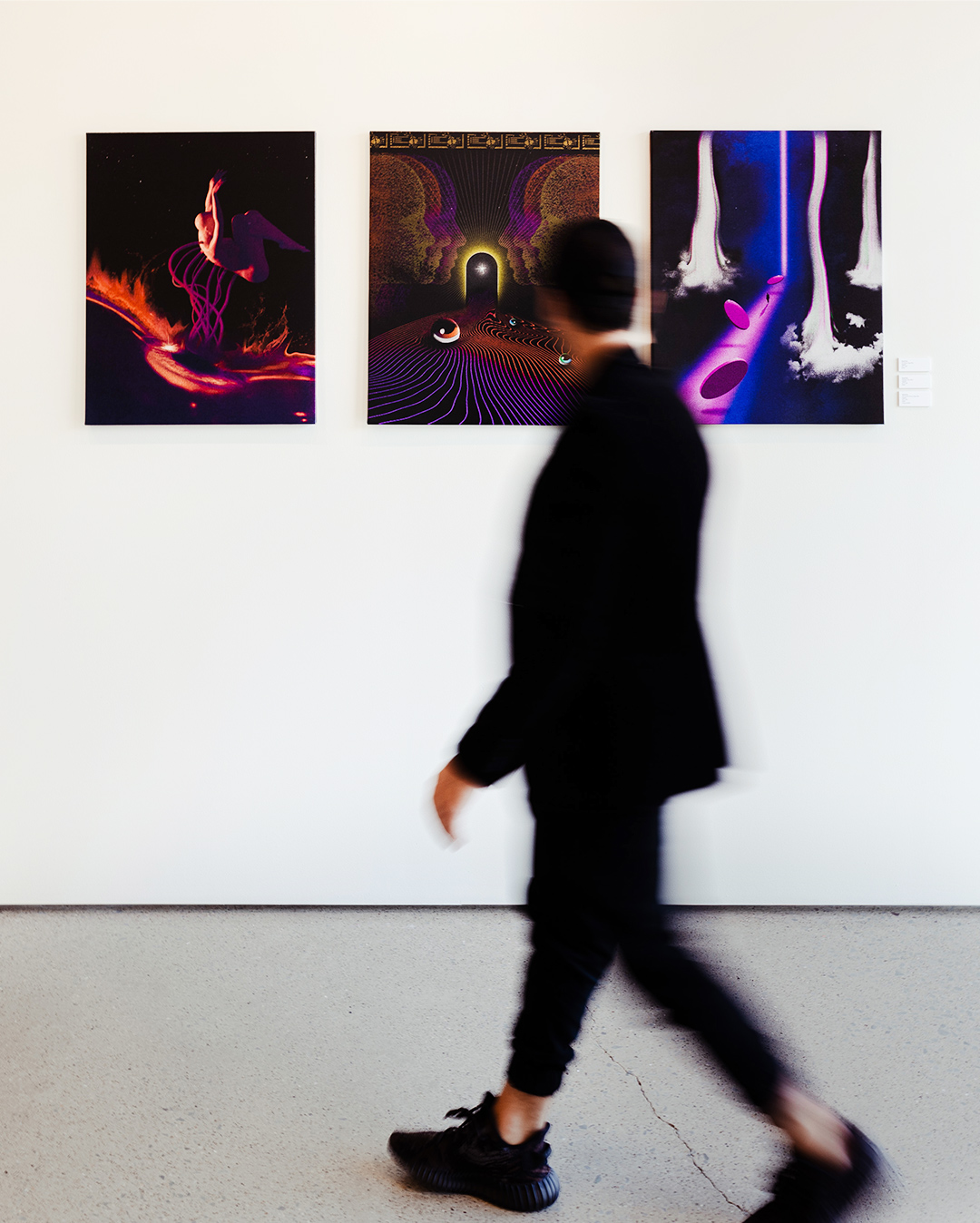 Image of a man in motion in an art gallery with three art installations in the background. 