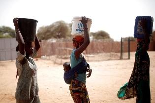 A person carrying a bucket on her head

Description automatically generated