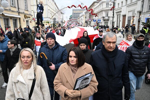 A crowd of people carrying a very long red-and-white flag through city streets.