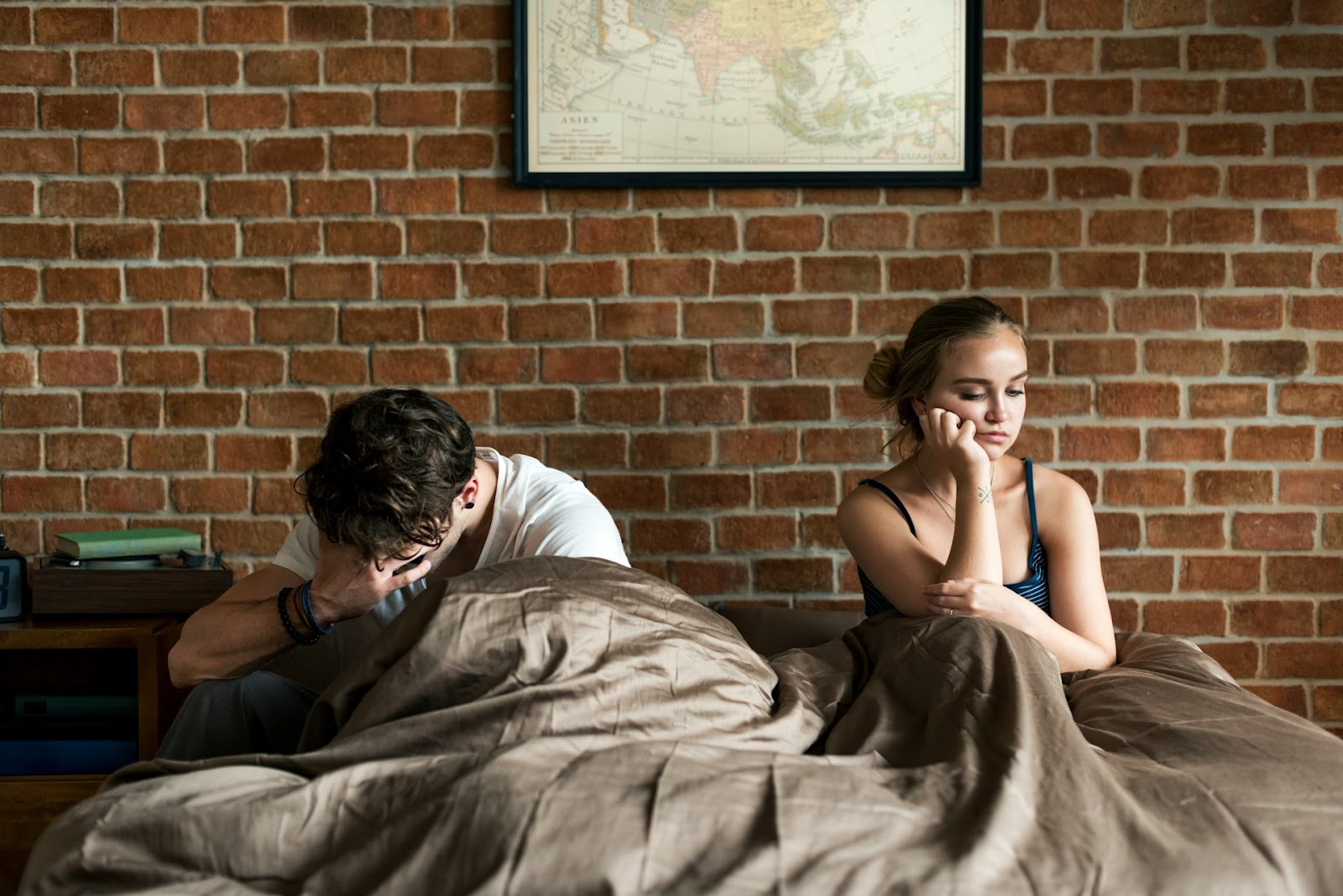 A couple sits in bed looking disappointed and upset after sex