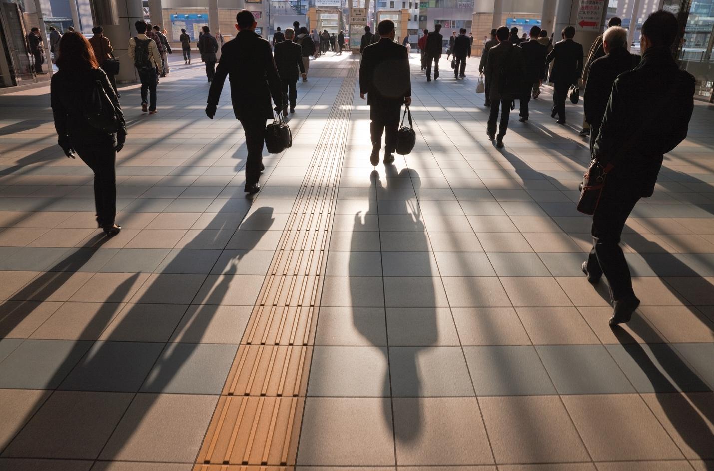 People in business wear, walking in train station lobby in daylight