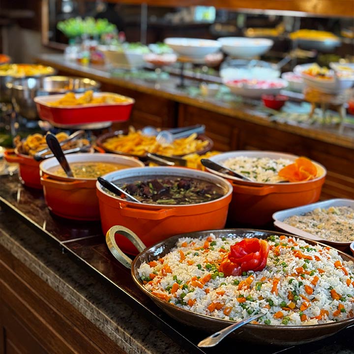 Variedade de pratos de culinária brasileira em buffet, incluindo arroz, feijão, saladas e acompanhamentos, em ambiente de restaurante com buffet self-service.