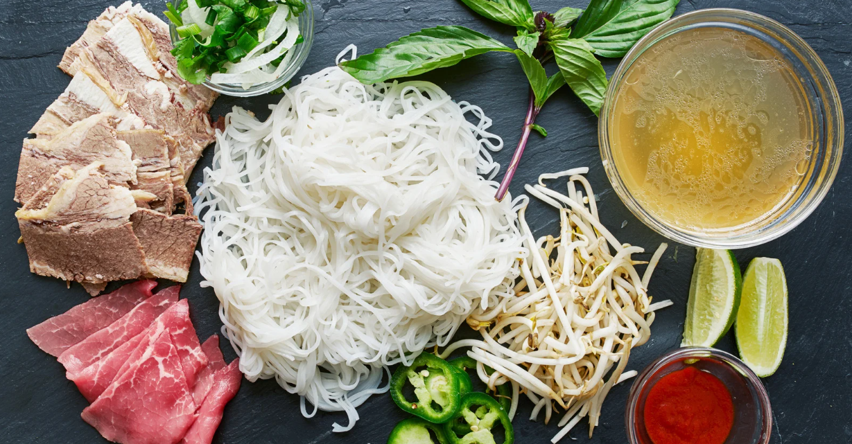 (Platte lay-out van pho-ingrediënten: noedels, rundvlees, kruiden, bouillon en garnering - vers en uitgebalanceerd.)