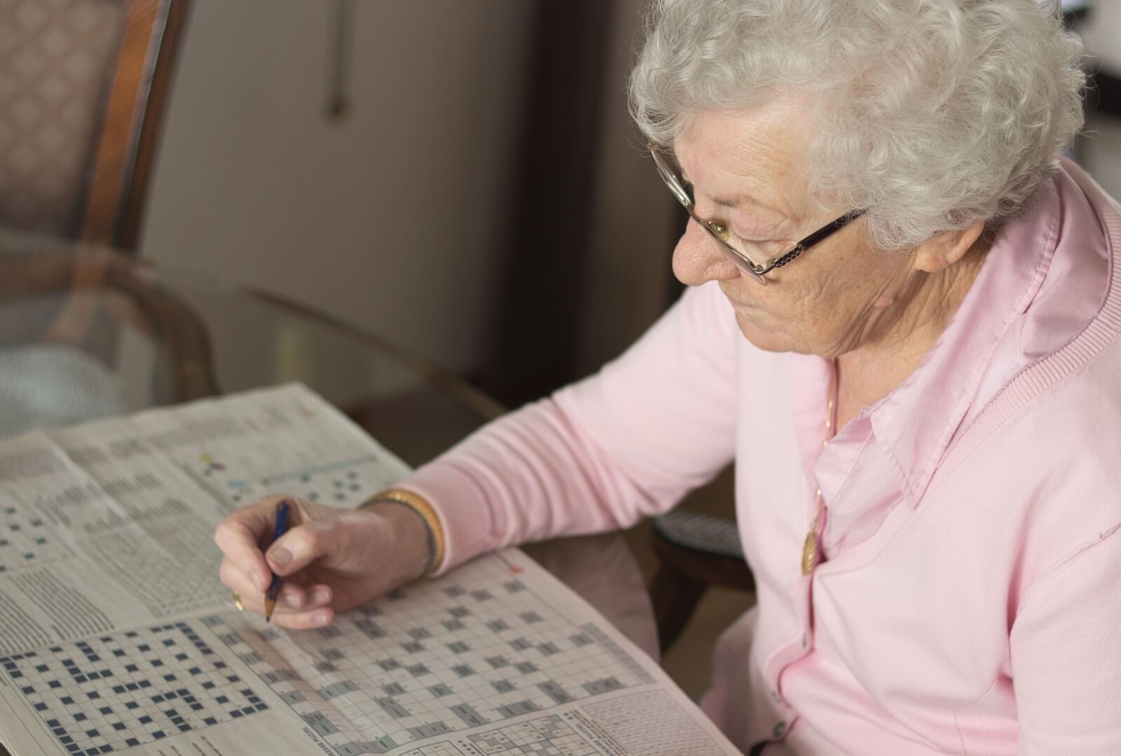 A senior woman enjoying a crossword puzzle at a senior living community.