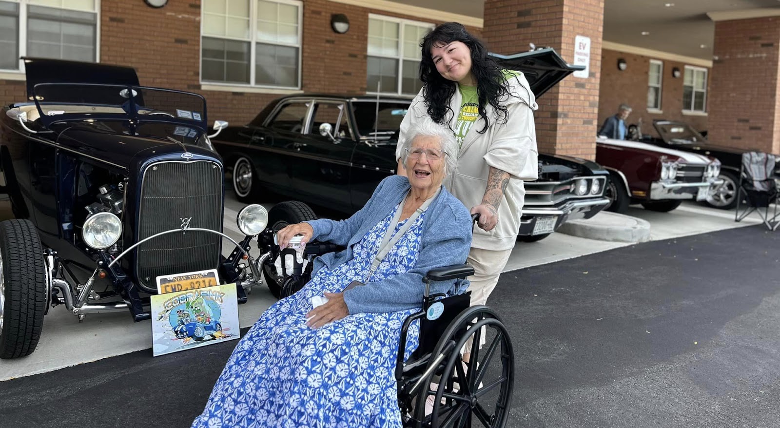 Two women smiling in front of old-style cars