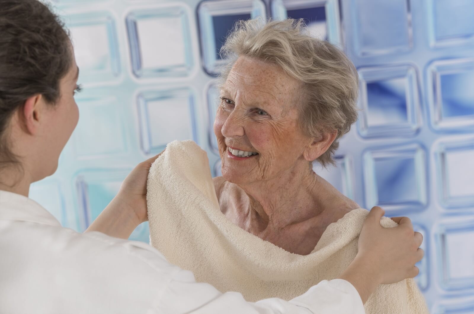 A caregiver covering a smiling older adult with a towel after a shower.