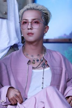 This contains an image of WINNER's Mino with glasses sitting down in front of a tv screen wearing a purple jacket