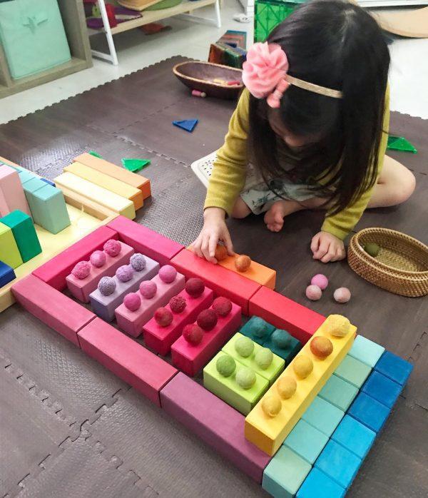 A toddler engaging in imaginative play with blocks and loose parts. The vibrant, multi-colored blocks are being used for colour sorting as the children arrange them into creative and unique structures.