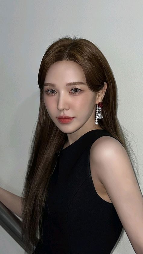 This contains an image of Wendywith long brown hair standing next to a white wall and wearing black dress