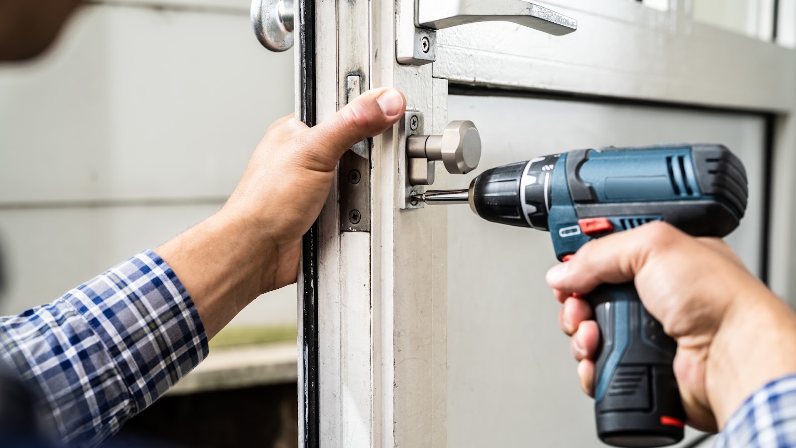 A technician fixing a broken door lock with a screwdriver and drill.