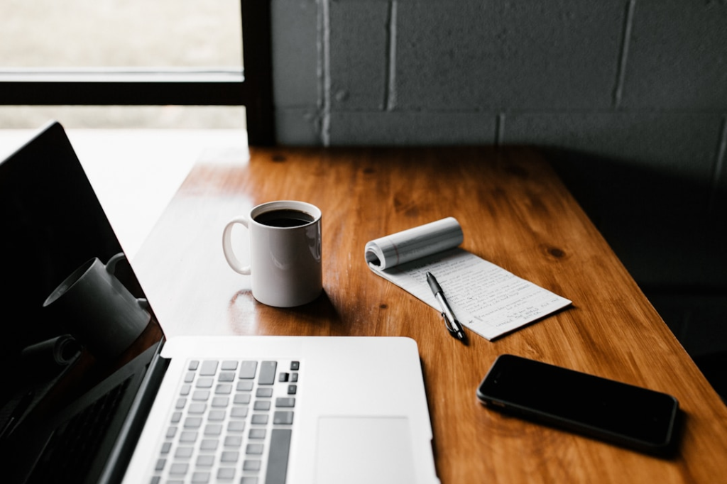 MacBook Pro, white ceramic mug,and black smartphone on table by Andrew Neel